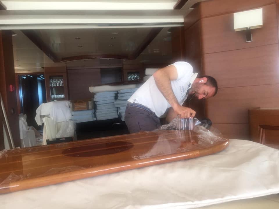 Technician polishing a varnished wooden surface inside a yacht.