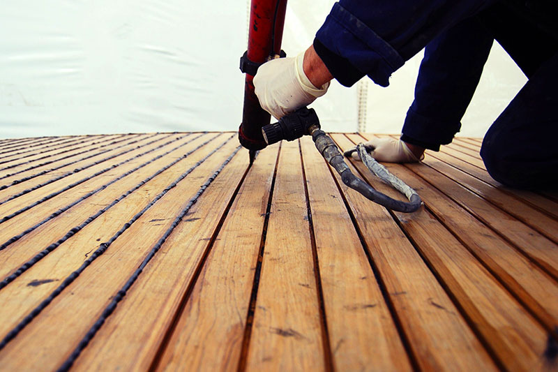 Close-up of a technician applying sealant between teak deck planks.