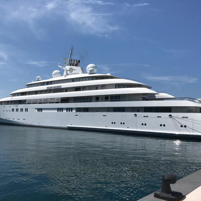 White superyacht berthed alongside a quay in bright sunlight.