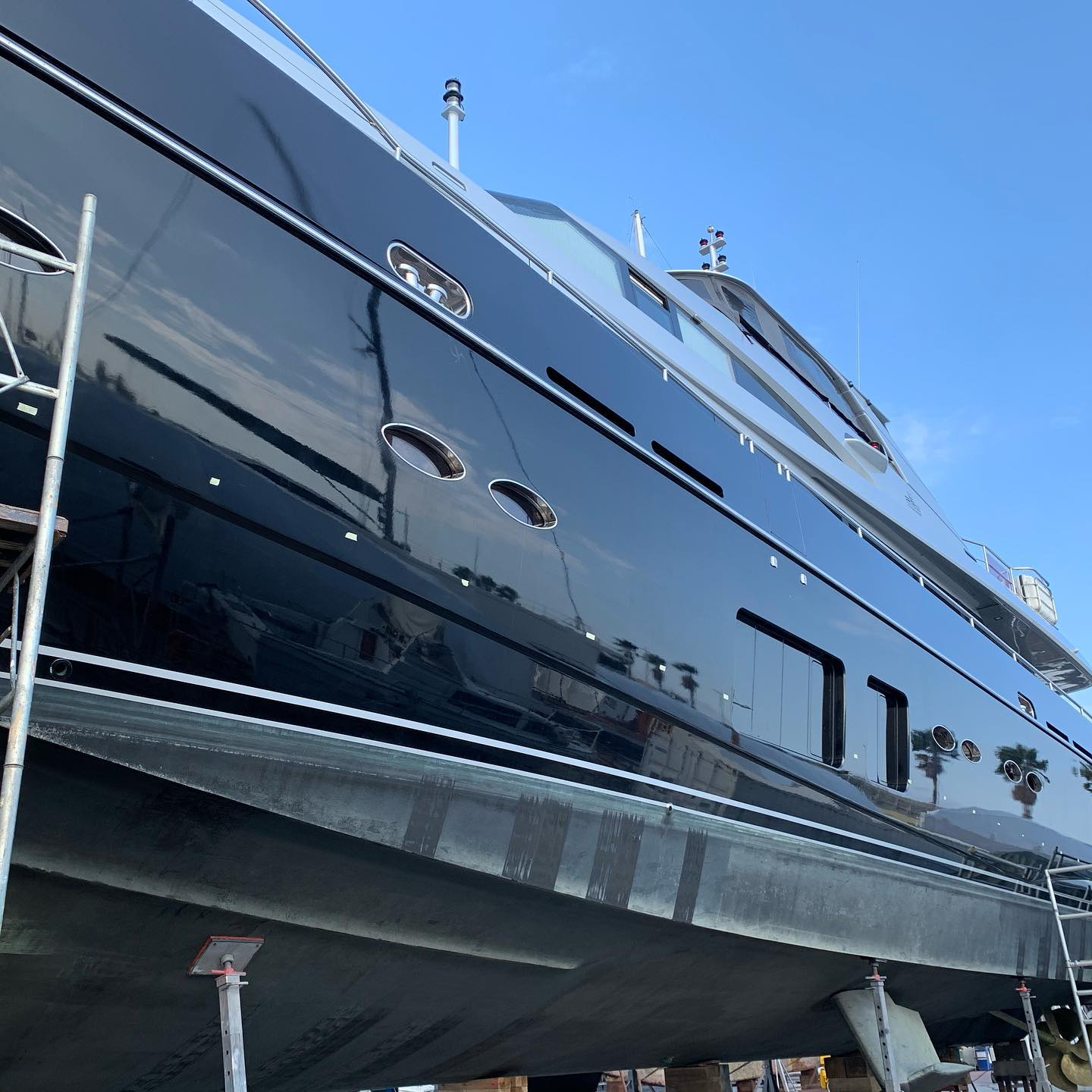 Glossy dark yacht hull in a shipyard behind scaffolding after wrapping.