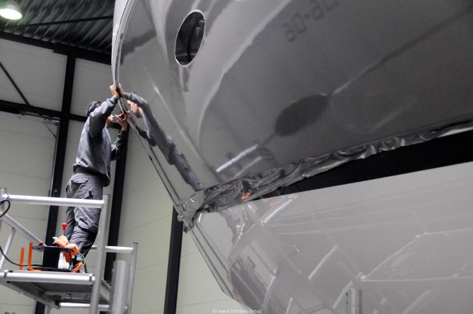 Two technicians applying protective film to a grey yacht hull.