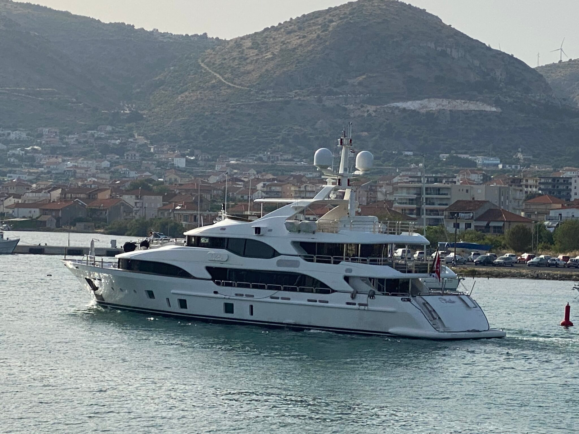Large white motor yacht under way along a green hillside coastline.