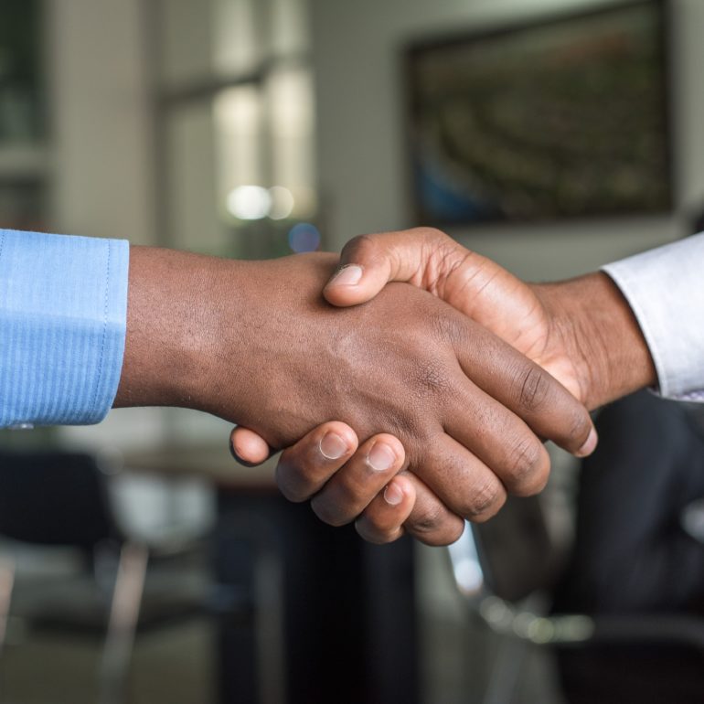 Two people shaking hands across a table in an office.