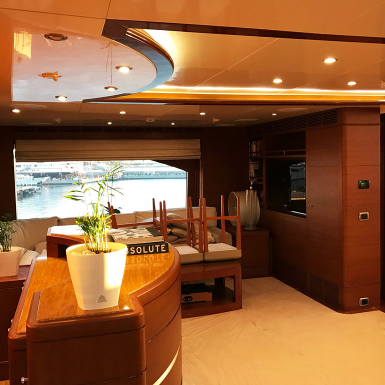 Warm wood-panelled yacht saloon with sofa, dining table and marina view.
